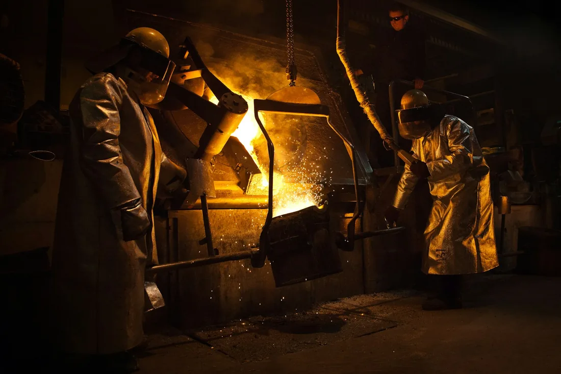 Dos operarios vierten metal fundido desde un crisol en un taller de fundición